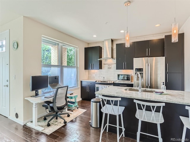 kitchen with wall chimney exhaust hood, a kitchen bar, hanging light fixtures, stainless steel appliances, and light stone countertops