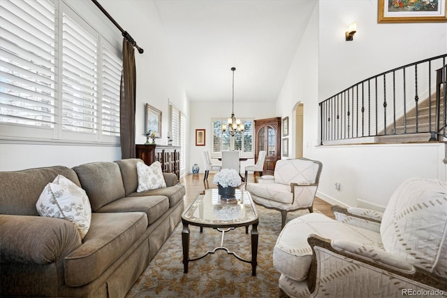 living area featuring arched walkways, stairway, wood finished floors, high vaulted ceiling, and a notable chandelier