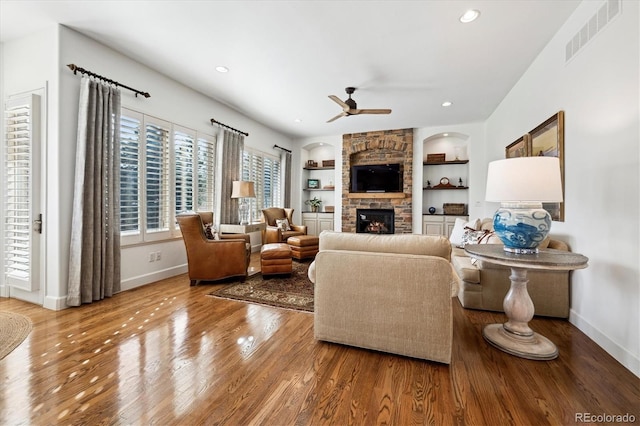 living area with baseboards, visible vents, wood finished floors, built in shelves, and a fireplace