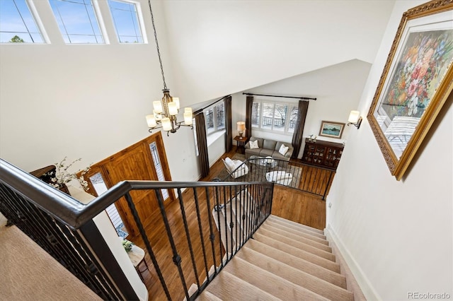 stairway with baseboards, high vaulted ceiling, a notable chandelier, and wood finished floors