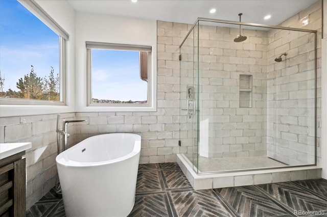 full bath featuring tile walls, recessed lighting, a freestanding bath, a stall shower, and vanity