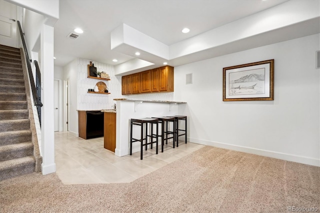 kitchen with a breakfast bar area, visible vents, light countertops, brown cabinetry, and a peninsula