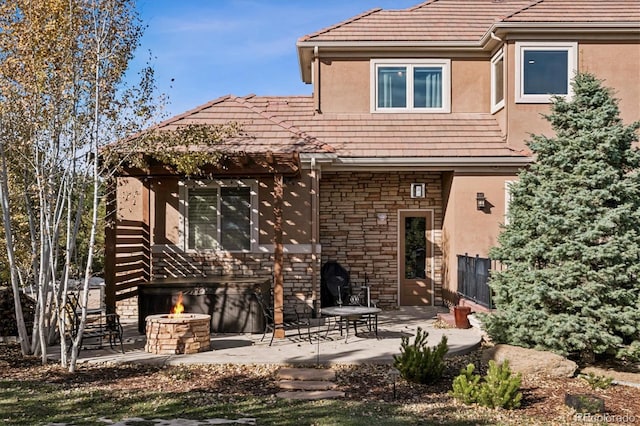 rear view of property featuring stone siding, an outdoor fire pit, a patio, and stucco siding