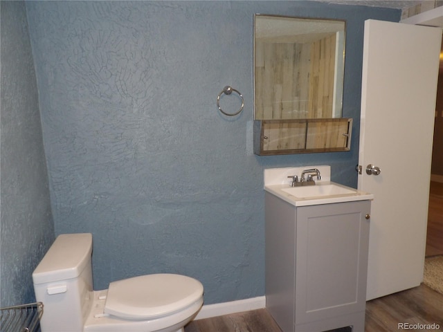 half bath featuring a textured wall, toilet, vanity, wood finished floors, and baseboards