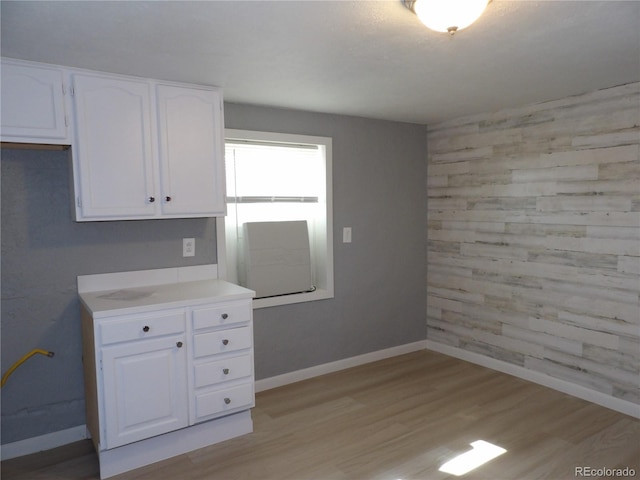 kitchen with light countertops, light wood-style flooring, white cabinets, wooden walls, and baseboards