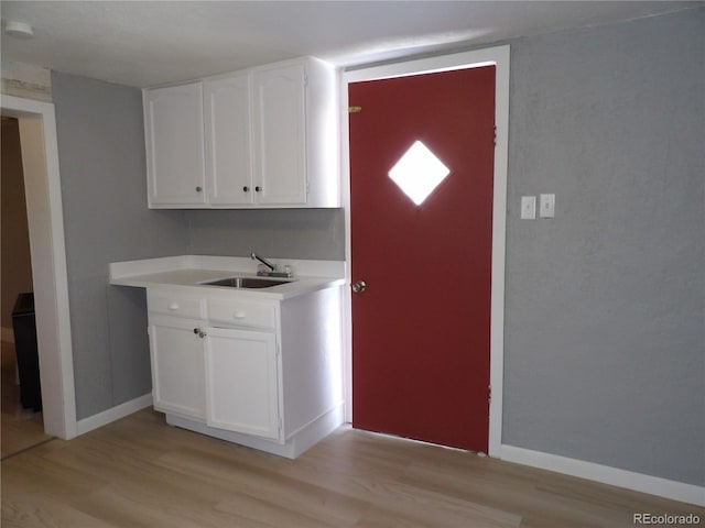 kitchen featuring light countertops, light wood finished floors, a sink, and white cabinets