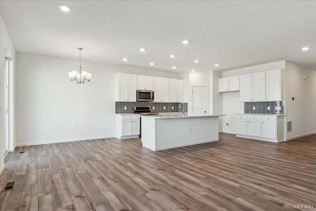 kitchen featuring decorative light fixtures, white cabinetry, light wood-type flooring, an island with sink, and stainless steel appliances