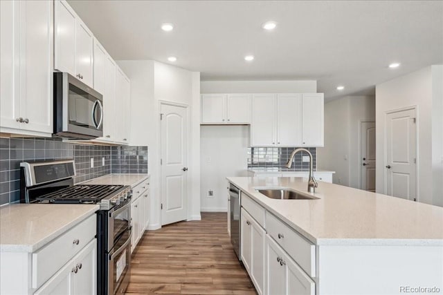 kitchen with decorative backsplash, sink, white cabinetry, a kitchen island with sink, and appliances with stainless steel finishes