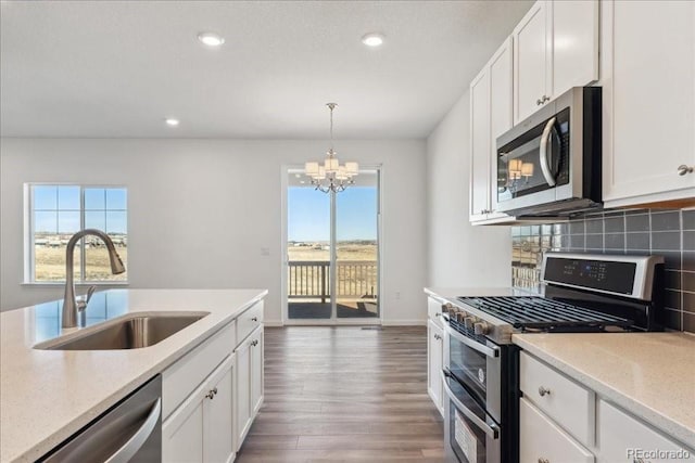 kitchen with tasteful backsplash, sink, white cabinetry, hanging light fixtures, and appliances with stainless steel finishes