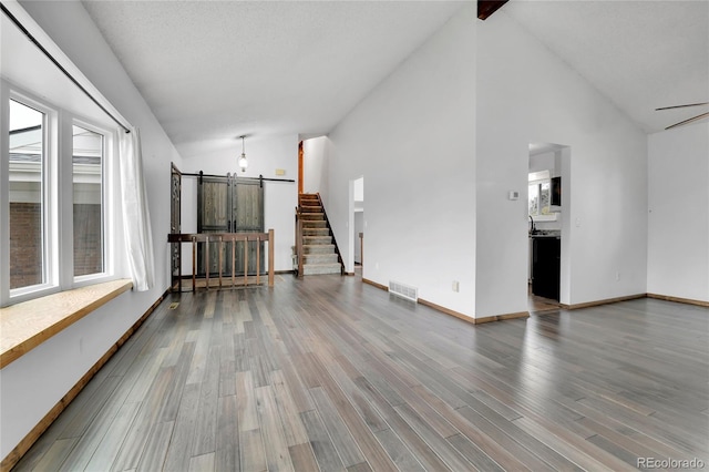 7796 S Marshall Ct, Littleton, CO 80128 - unfurnished living room with a barn door, plenty of natural light, wood finished floors, and high vaulted ceiling