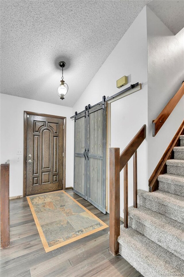 7796 S Marshall Ct, Littleton, CO 80128 - foyer entrance with wood finished floors, vaulted ceiling, a textured ceiling, stairs, and a barn door