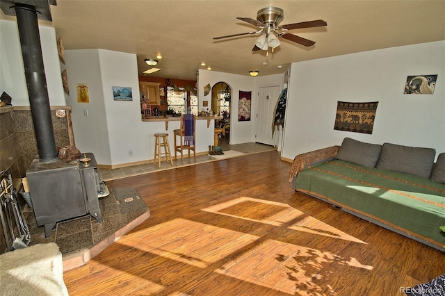 living room featuring ceiling fan, hardwood / wood-style flooring, and a wood stove