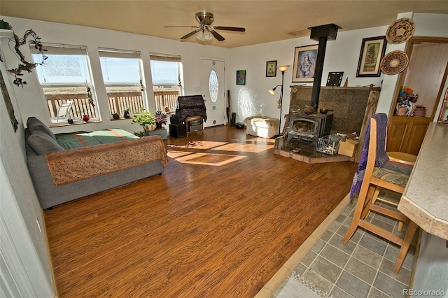 living room featuring a wood stove, ceiling fan, and wood-type flooring