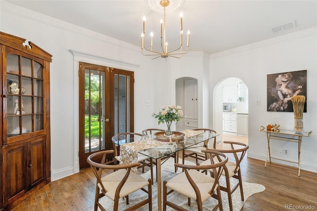 dining room with hardwood / wood-style flooring, a chandelier, crown molding, and french doors