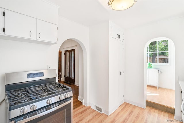 kitchen with light hardwood / wood-style flooring, crown molding, white cabinets, and stainless steel gas range oven