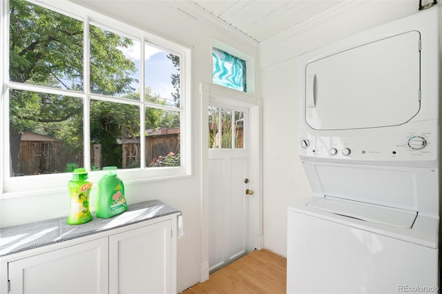 laundry room featuring cabinets, stacked washer / dryer, crown molding, and light hardwood / wood-style floors