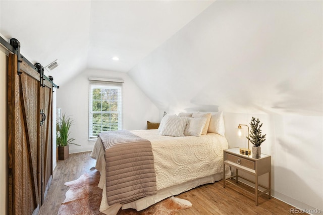 bedroom featuring hardwood / wood-style floors, vaulted ceiling, and a barn door