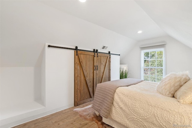 bedroom featuring a barn door, wood-type flooring, and lofted ceiling