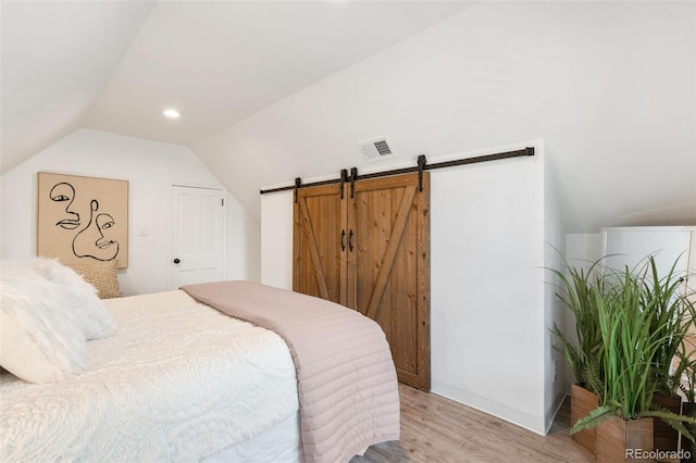 bedroom with light wood-type flooring, lofted ceiling, and a barn door