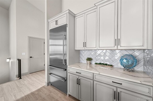 kitchen featuring built in refrigerator, decorative backsplash, and light stone counters