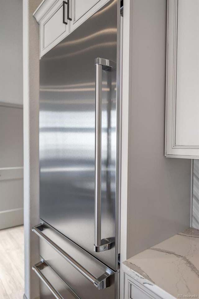 room details with white cabinets, built in fridge, and light stone countertops