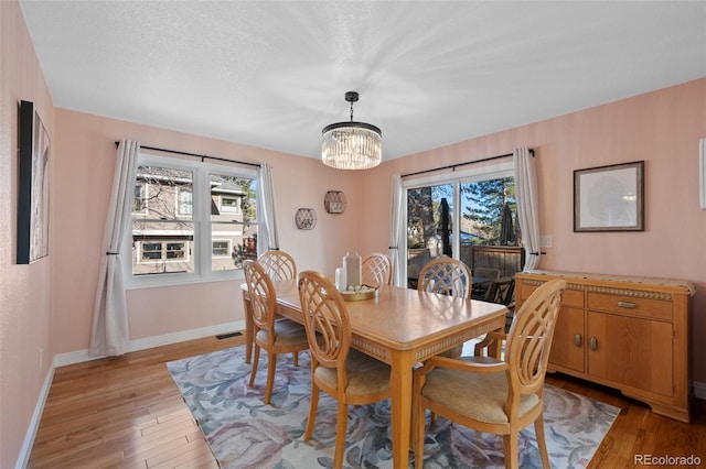 dining area featuring light hardwood / wood-style flooring, a textured ceiling, and an inviting chandelier