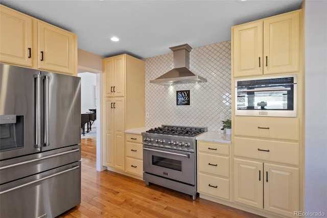 kitchen featuring decorative backsplash, stainless steel appliances, wall chimney range hood, and light hardwood / wood-style floors