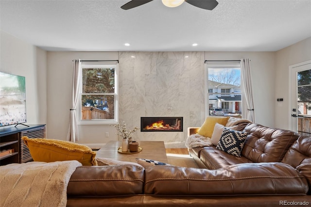 living room with a textured ceiling, ceiling fan, and a fireplace