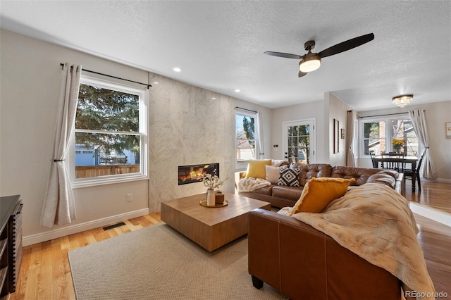 living room featuring a wealth of natural light, ceiling fan, a fireplace, and light hardwood / wood-style flooring