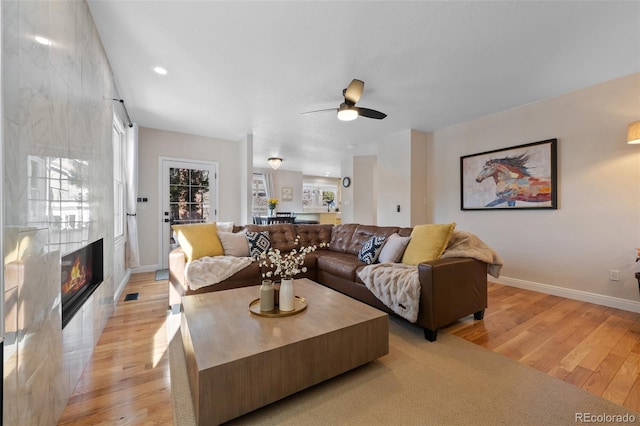 living room featuring light wood-type flooring, ceiling fan, a healthy amount of sunlight, and a tiled fireplace