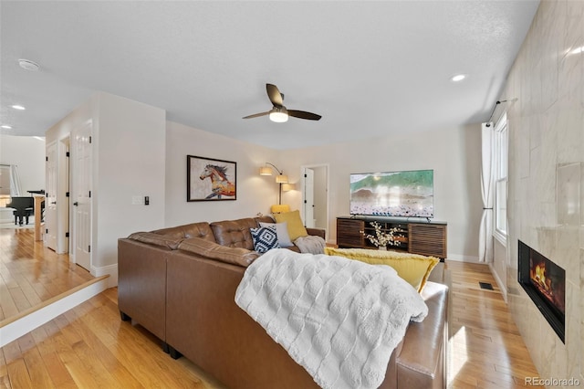 living room with a tile fireplace, ceiling fan, and light hardwood / wood-style flooring