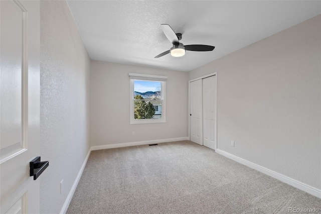 unfurnished bedroom with carpet flooring, ceiling fan, a closet, and a textured ceiling