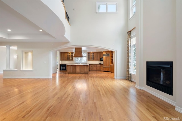4800 E Cedar Ave, Denver, CO 80246 - unfurnished living room featuring light wood-type flooring, arched walkways, a glass covered fireplace, a high ceiling, and baseboards