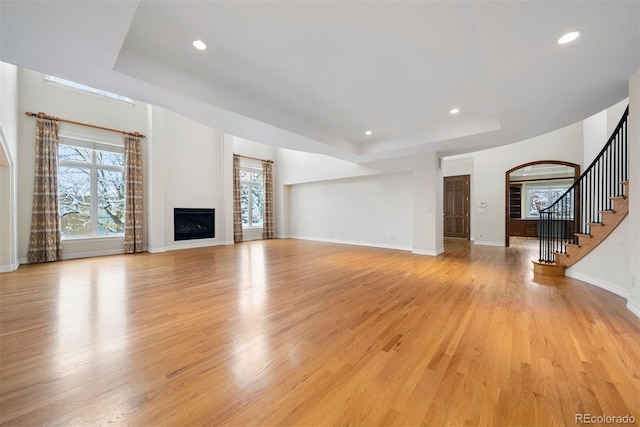 4800 E Cedar Ave, Denver, CO 80246 - unfurnished living room featuring a tray ceiling, arched walkways, a fireplace, light wood-style floors, and stairs