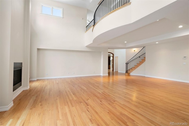 4800 E Cedar Ave, Denver, CO 80246 - unfurnished living room with stairway, arched walkways, light wood finished floors, recessed lighting, and a glass covered fireplace