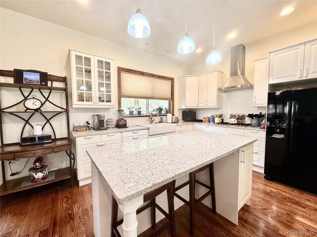 185 Wildrose Ct, Woodland Park, CO 80863 - kitchen with black fridge with ice dispenser, wall chimney range hood, a center island, decorative backsplash, and a kitchen breakfast bar