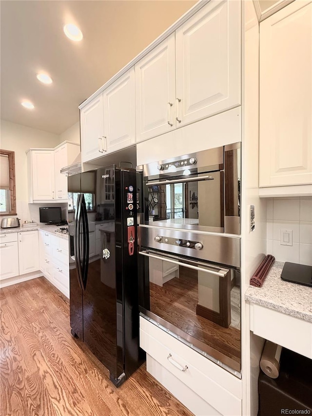 185 Wildrose Ct, Woodland Park, CO 80863 - kitchen with black fridge with ice dispenser, double oven, white cabinets, recessed lighting, and decorative backsplash
