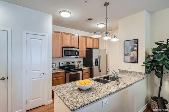 kitchen with stainless steel appliances, a sink, a peninsula, light wood-style flooring, and light stone countertops