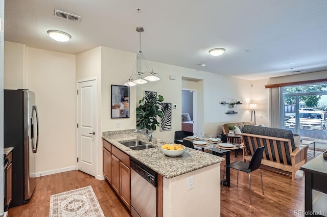 kitchen with stainless steel appliances, a sink, light wood-type flooring, brown cabinetry, and a peninsula