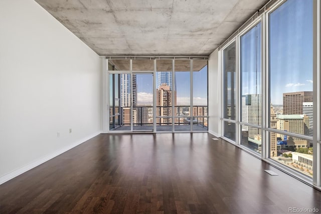 spare room featuring floor to ceiling windows, a view of city, baseboards, and wood finished floors