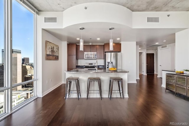 kitchen with a kitchen bar, decorative light fixtures, stainless steel appliances, and dark wood-type flooring