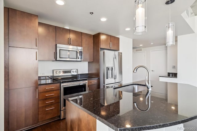 kitchen featuring stainless steel appliances, a kitchen island with sink, sink, pendant lighting, and dark stone countertops