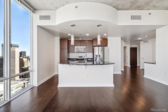 kitchen with dark hardwood / wood-style floors, a kitchen island with sink, stainless steel appliances, and hanging light fixtures