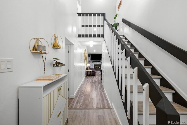hallway featuring stairs, baseboards, wood finished floors, and a towering ceiling