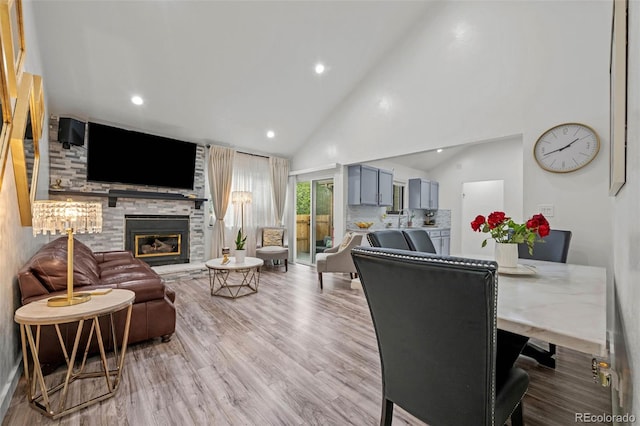 living room featuring recessed lighting, high vaulted ceiling, a stone fireplace, and wood finished floors