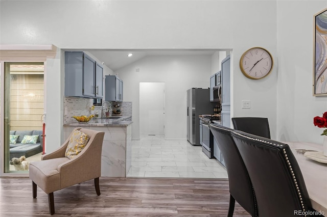 kitchen featuring appliances with stainless steel finishes, tasteful backsplash, light stone countertops, a sink, and lofted ceiling