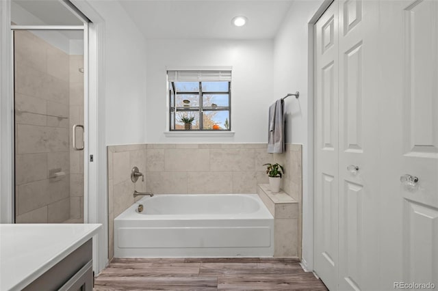 bathroom with a shower stall, recessed lighting, a bath, and wood finished floors