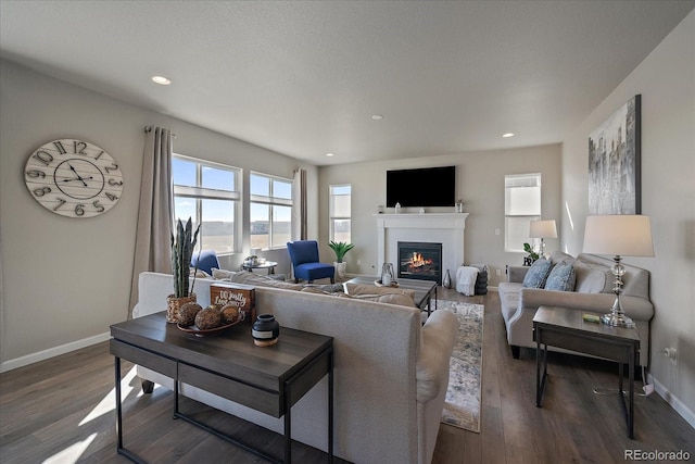 living room featuring a glass covered fireplace, recessed lighting, dark wood-type flooring, and baseboards