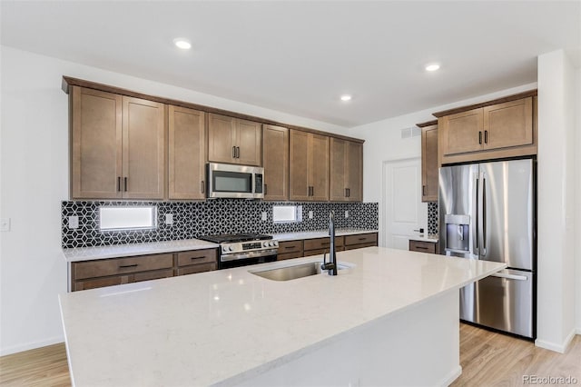 4451 Soapberry Pl, Castle Rock, CO 80108 - kitchen with appliances with stainless steel finishes, tasteful backsplash, a center island with sink, light wood-style flooring, and recessed lighting
