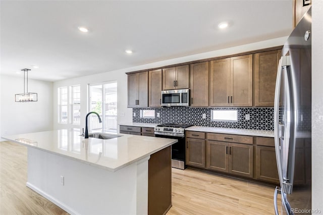4451 Soapberry Pl, Castle Rock, CO 80108 - kitchen with appliances with stainless steel finishes, decorative backsplash, light wood finished floors, light countertops, and a center island with sink